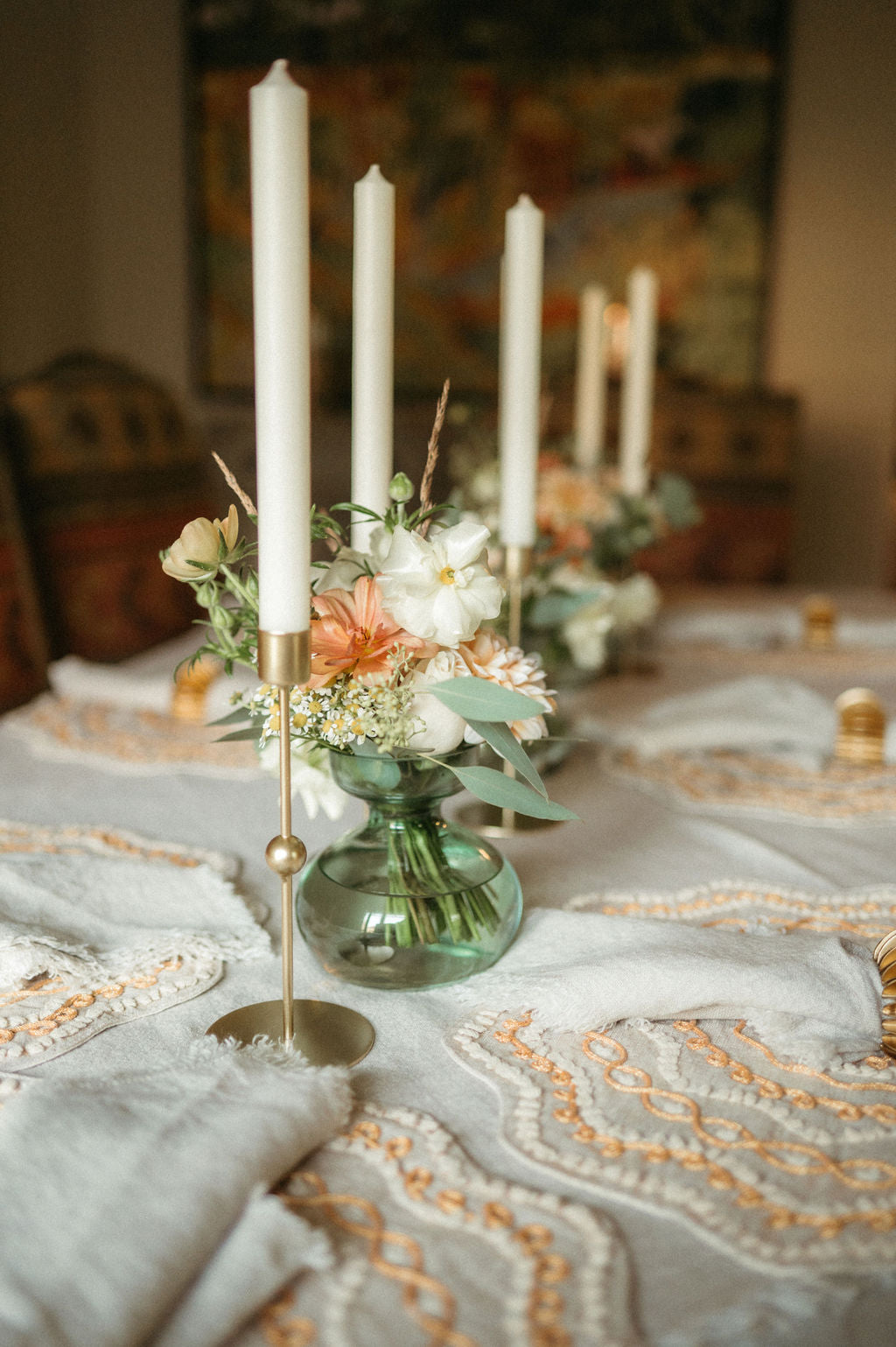 Decorative table setting with candles, flowers, and a vase on a tablecloth.