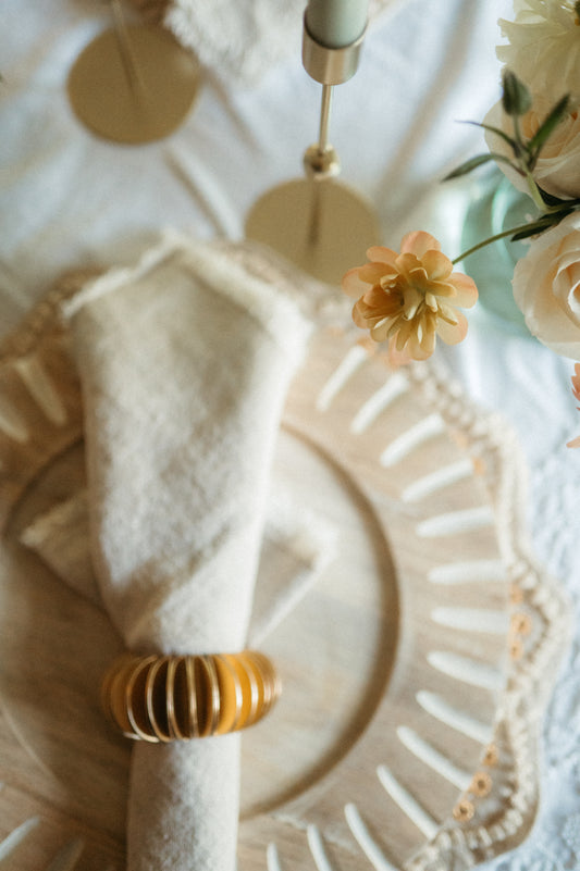Decorative plate with a white napkin and gold ring on a textured surface with flowers.