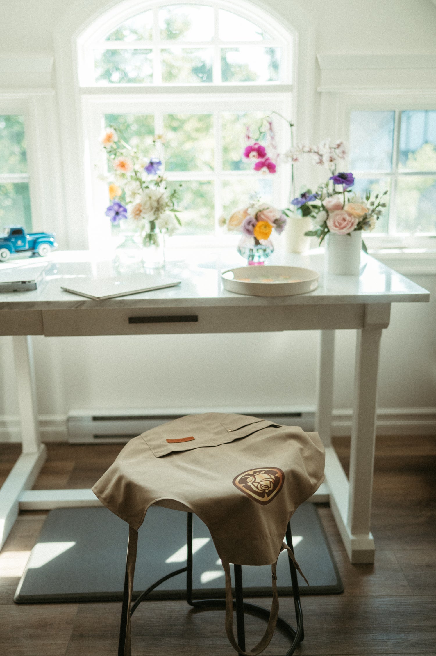 White table with a chair draped with a beige cloth in a bright room with large windows.