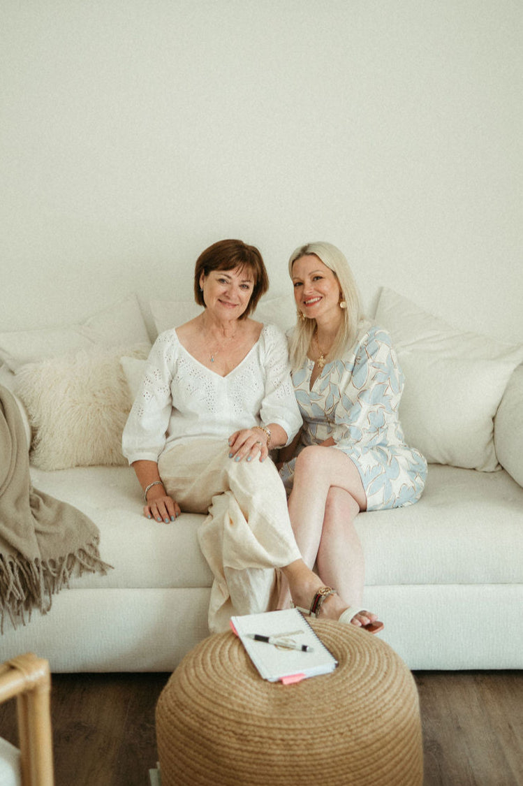 Two women sitting on a white couch in a minimalistic room.
