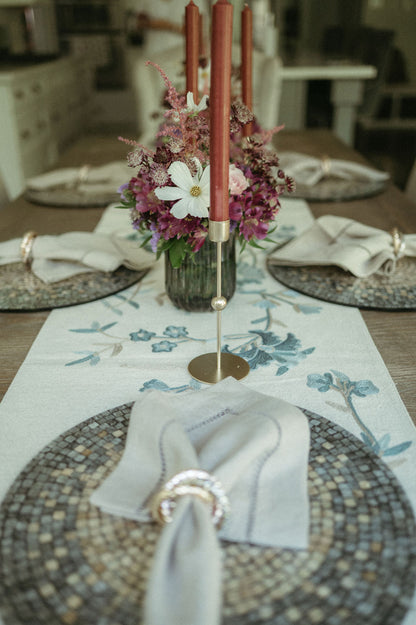 Dining table setting with floral centerpiece, candles, and patterned placemats.