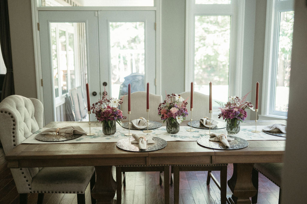 Dining table set for a meal with place settings, candles, and floral arrangements.