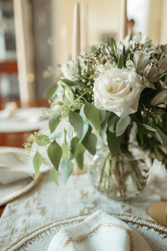 Bouquet of white roses and greenery in a clear vase on a table with a blurred background