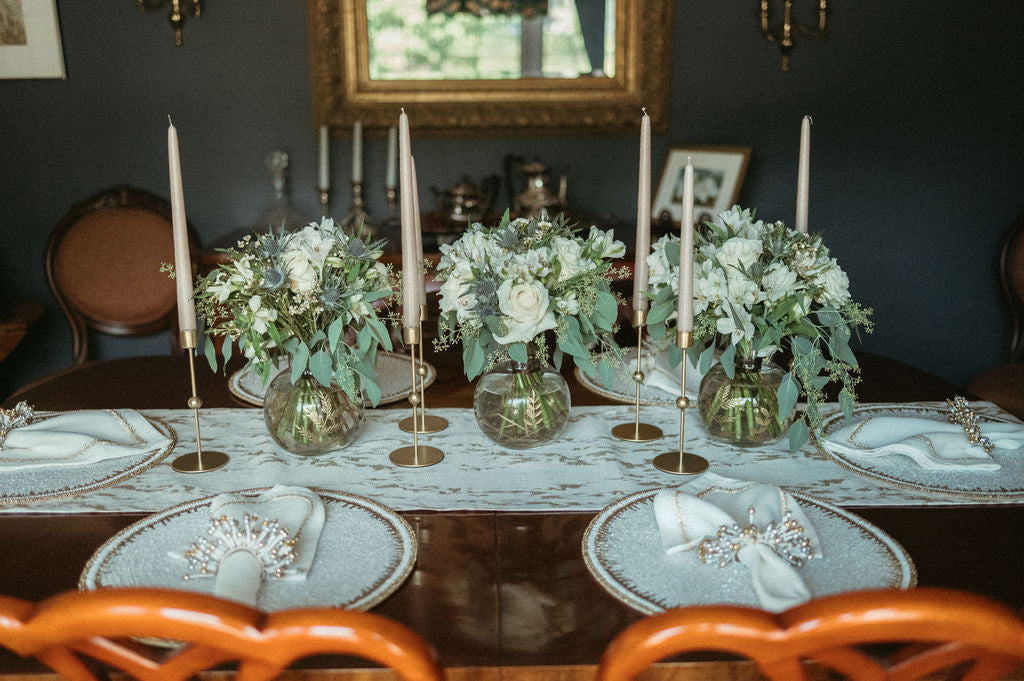 Dining table set with floral centerpieces, candles, and place settings in a formal dining room.