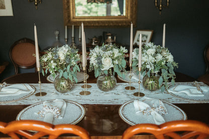 Dining table set with floral centerpieces, candles, and place settings in a formal dining room.