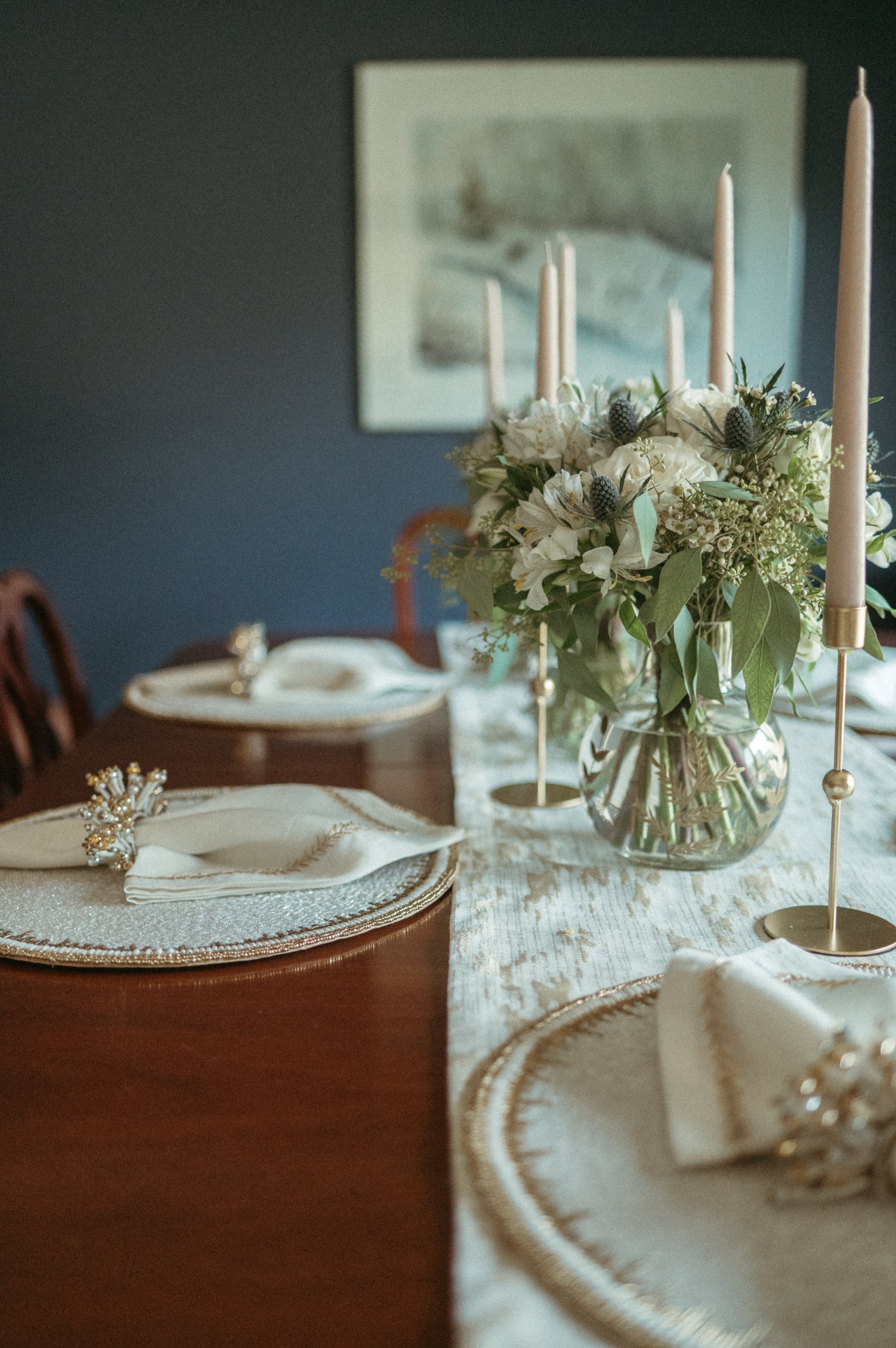 Dining table set with floral centerpiece, candles, and decorative plates against a dark wall.