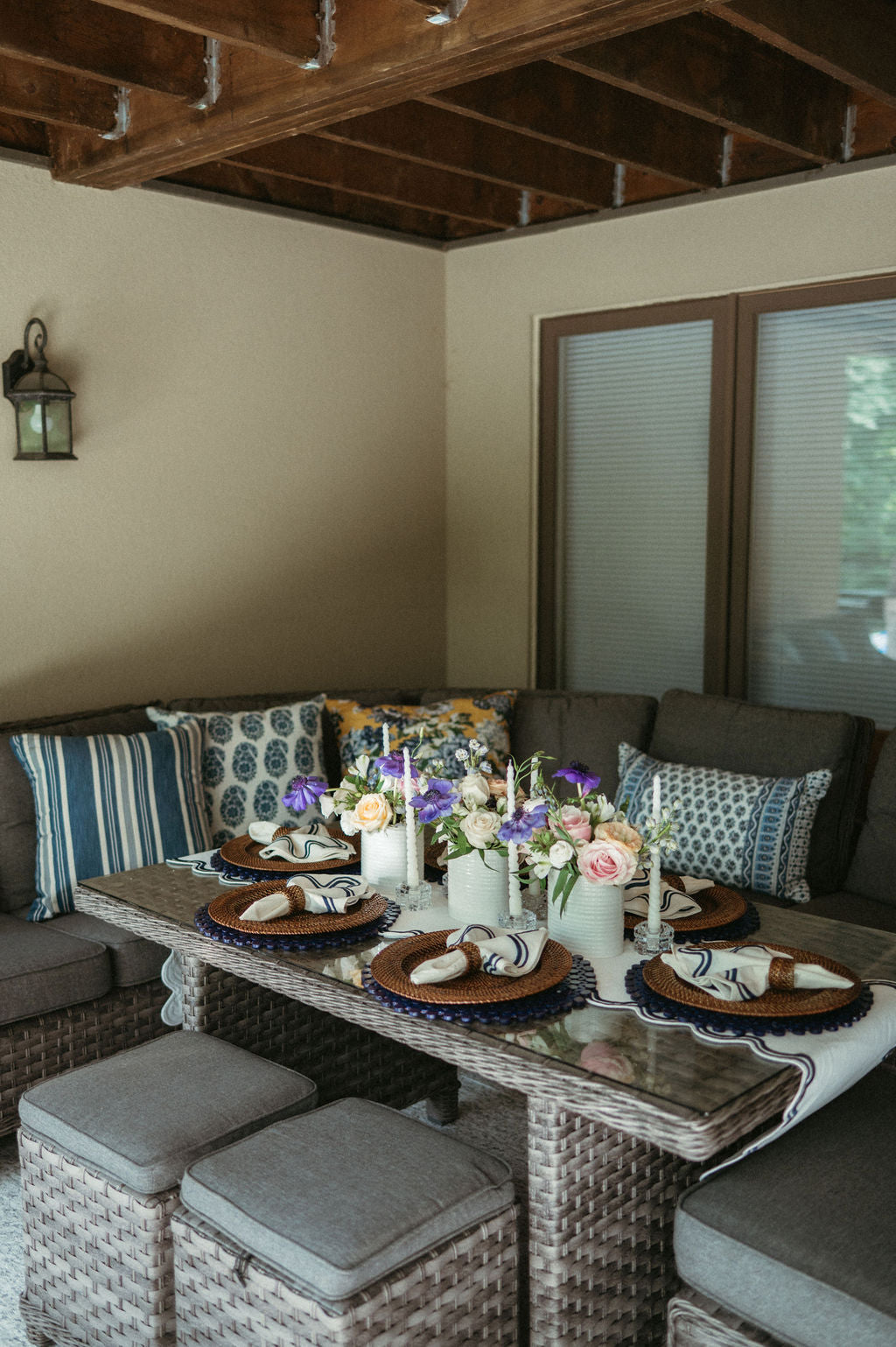 Dining area with a table set for a meal, featuring plates, napkins, and candles, with a couch and cushions in the background.