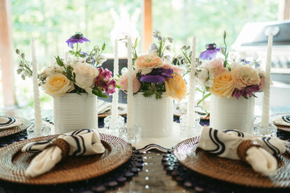 Decorative table setting with floral centerpieces, candles, and woven plates.
