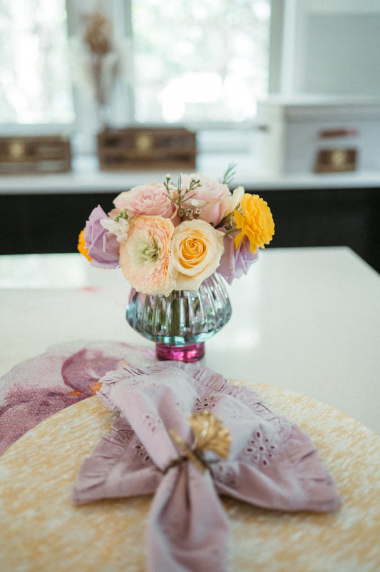 Small bouquet of flowers in a colorful vase on a table with a decorative cloth.