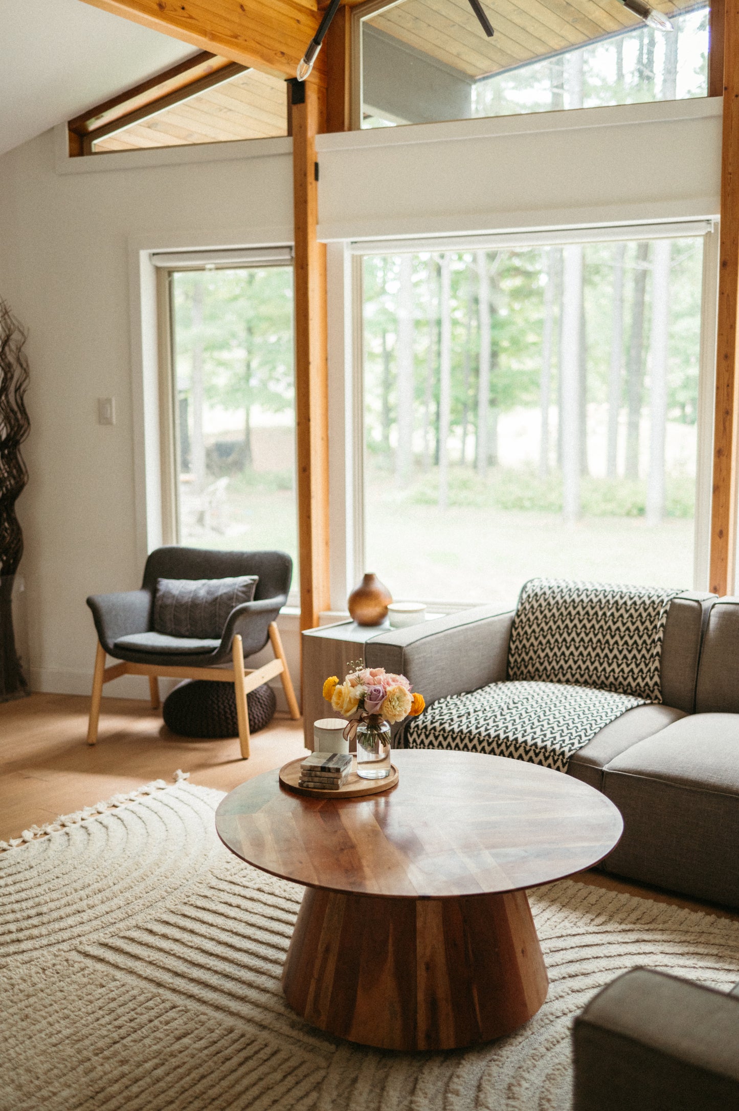 Modern living room with a wooden coffee table, sofa, and chairs with a view of trees outside.
