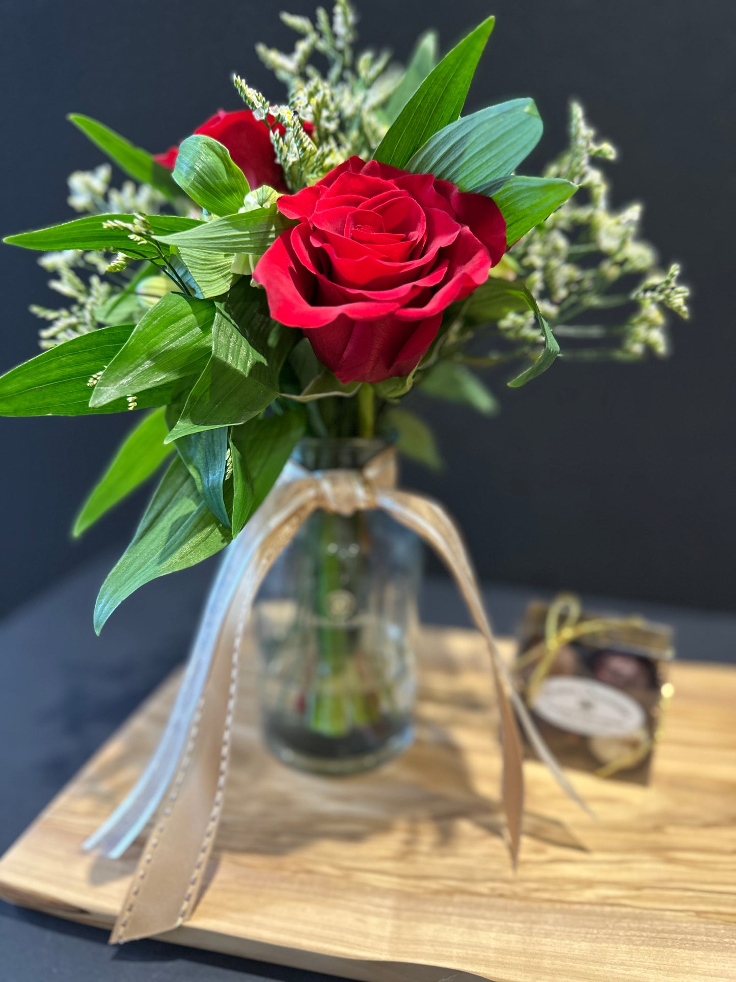Bouquet of red roses in a bloom vase with green leaves on a charcuterie board.