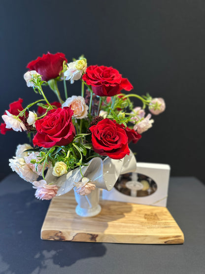 Bouquet of red and white flowers on a charcuterie board, with chocolate, with a dark background